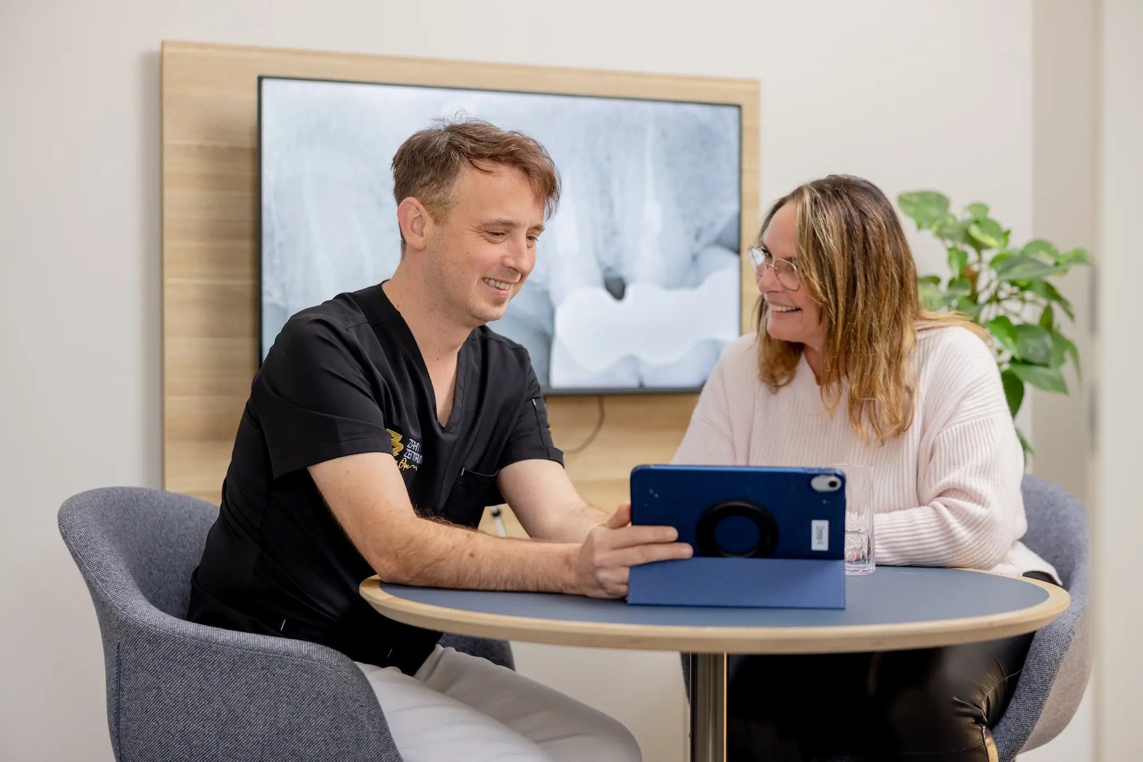 Beratungsgespräch am Tablet: Zahnarzt Torsten Hotzler erklärt einer Patientin die Behandlung im Zahnzentrum Olpe